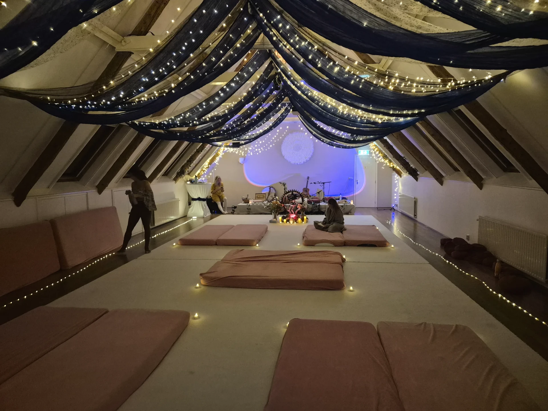 un comble sous voilage et guirlandes, des futons alignés